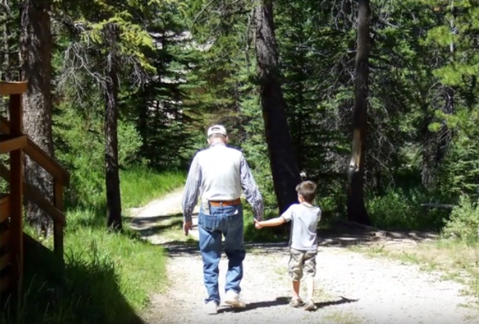 A color image of an older man holding hands with a child. They are walking outside.