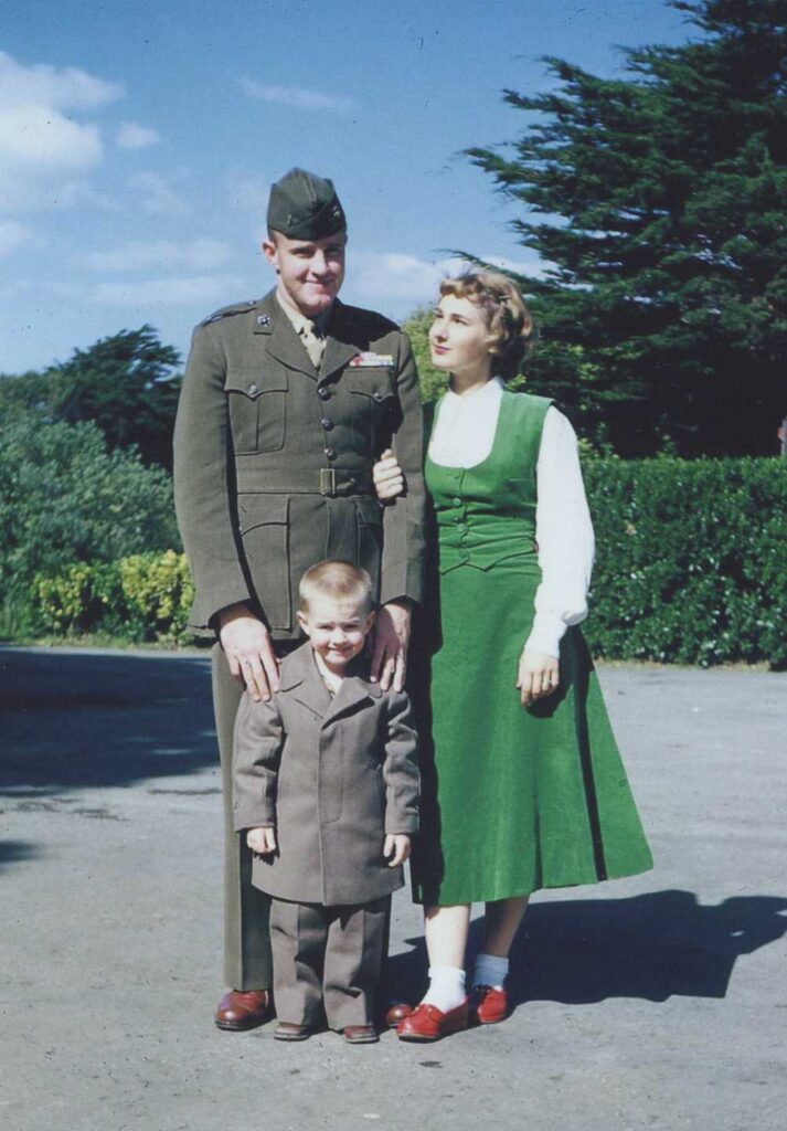 A color image of a young White man and woman standing with their child outside.