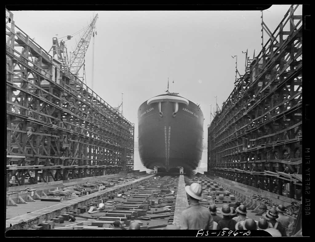 A black and white image of a ship leaving the building scaffolding.