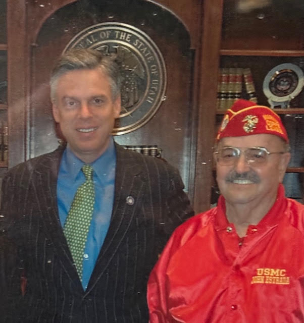 A color image of two men. One in a suit and tie. One in a red jacket and uniform cap.