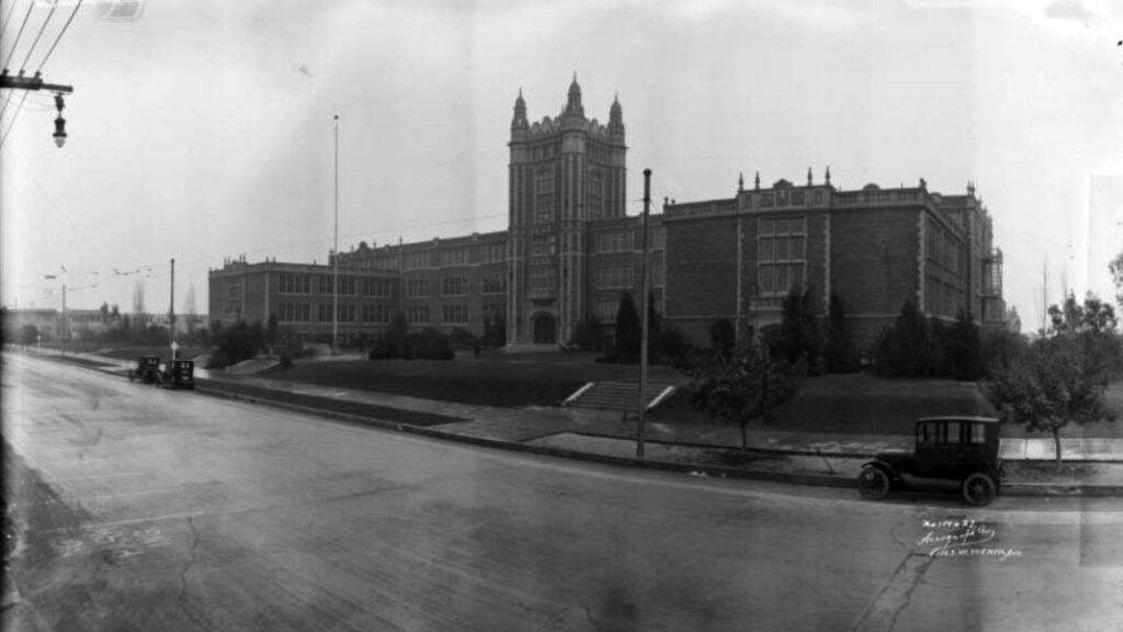 A black and white image of a large brick school building with several stories.
