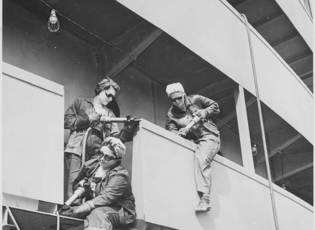 A black and white image of several women welding on a ship.