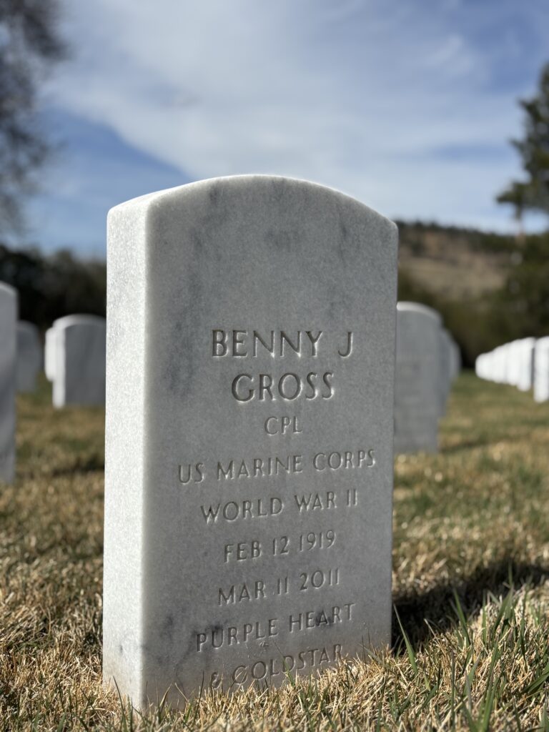 A color image of an arched white marble headstone engraved with "Benny J Gross CPL US Marine Corps World War II Feb 12 1919 Mar 11 2011 Purple Heart & Gold Star."