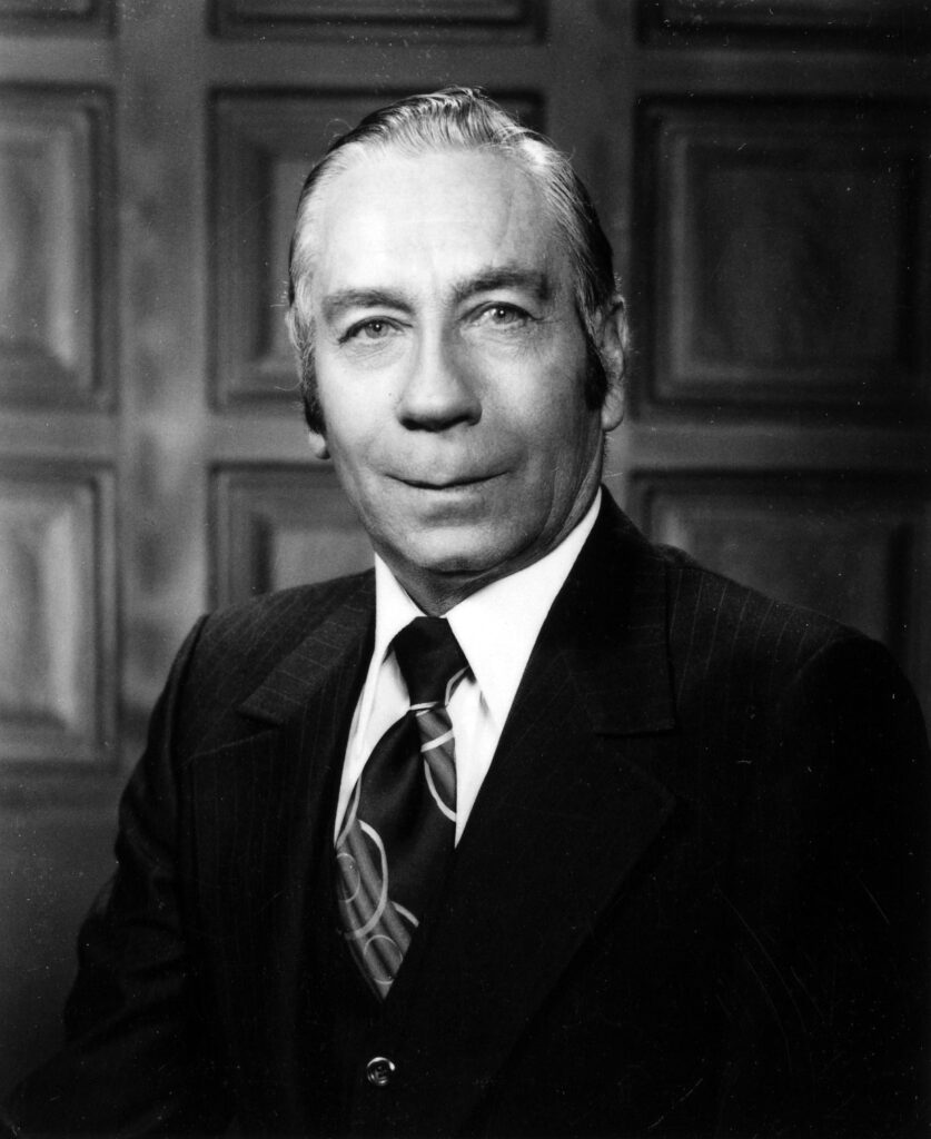 A black and white headshot image of an older White man in a suit and tie.