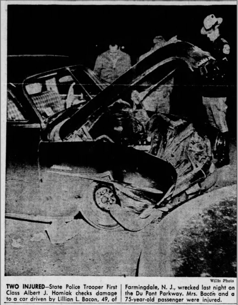 A black and white photo with a caption description. The photo shows a police trooper in uniform outside a car that has crashed. There are two others standing outside the crash.