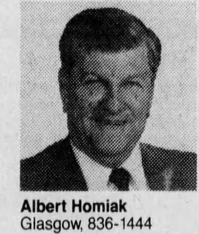 A black and white headshot image of an older White man in a suit and tie. The caption reads, “Albert Homiak Glasgow, 836-1444.”