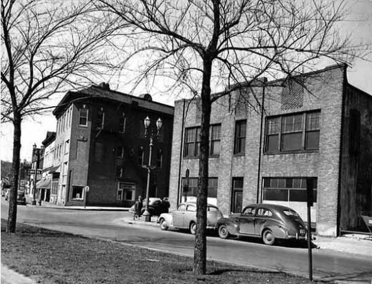 A black and white image of a three-story brick building next to a two-story brick building.