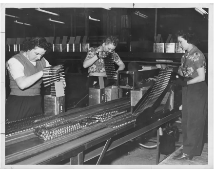 A black and white photo of three women packing ammunition at a factory.