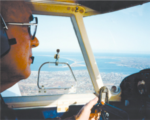 A color photograph of an older White man at the cockpit of a plane in the air.