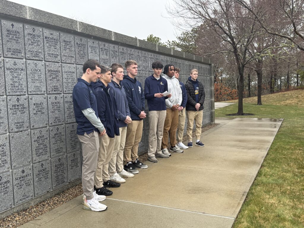 A color photo of several young men standing in front of a columbaria.