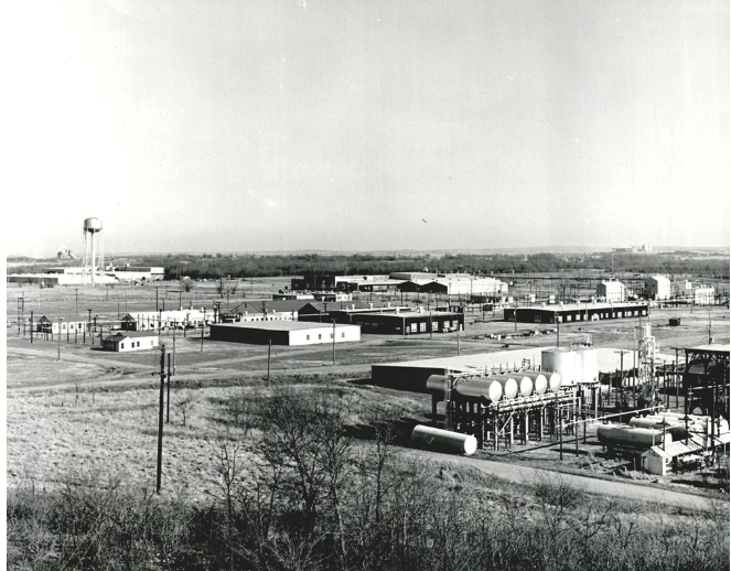A black and white aerial photograph of several factory buildings in a rural setting.