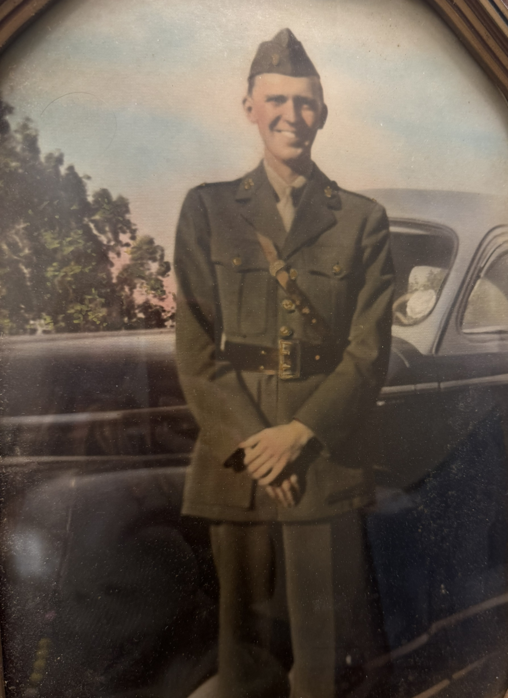 A young man in military uniform standing in front of a car.