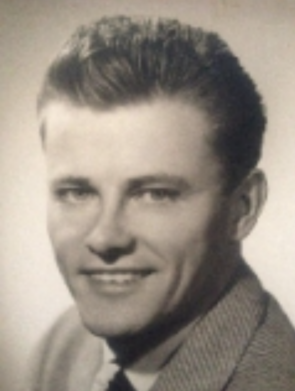 A black and white headshot of a young White man in a suit and tie.