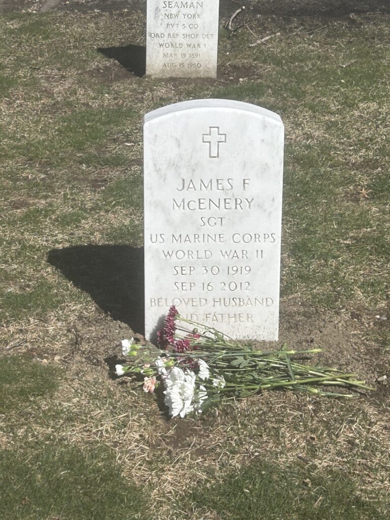 A color image of an arched white marble headstone engraved with a cross and “James F McEnery SGT U.S. Marine Corps World War II Sep 30 1919 Sep 16 2012 Belowed Husband and Father.”