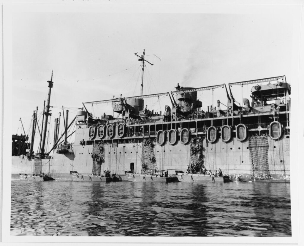 A black and white image of the side of a ship with many troops coming down the side into smaller boats.