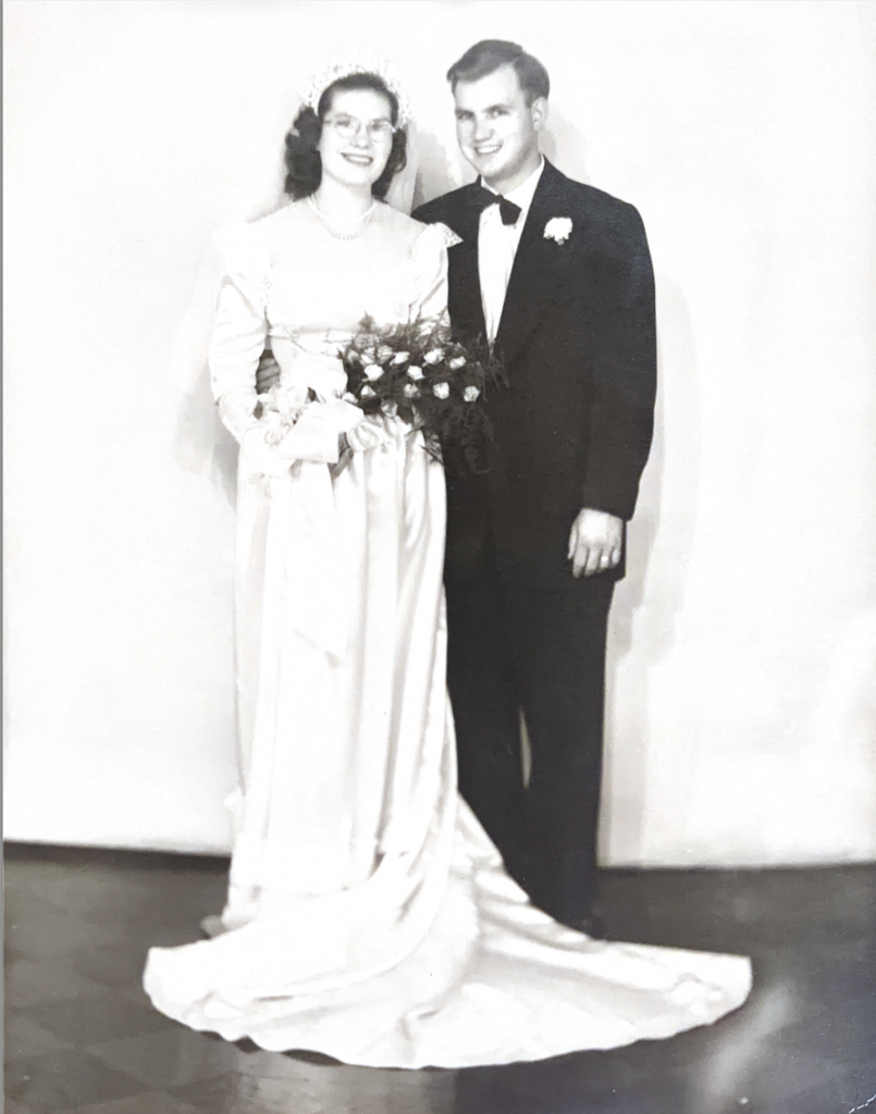 A black and white wedding photo featuring a young White man and woman in a wedding gown and suit and tie. 