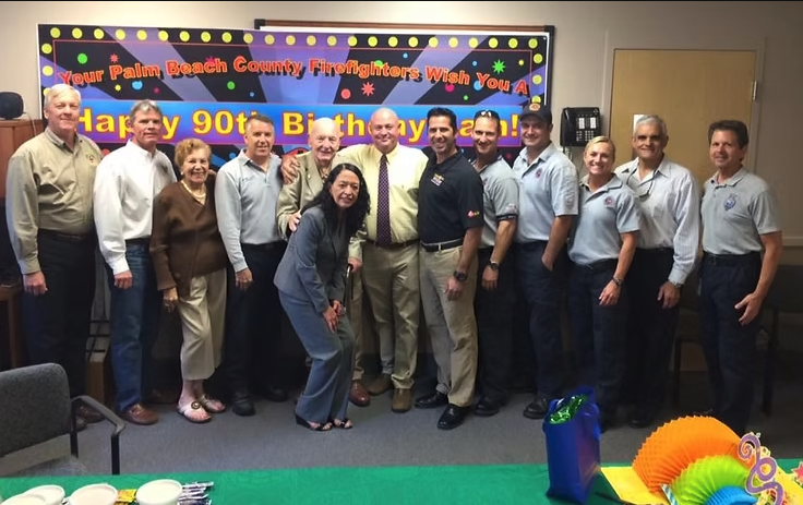 A color image of several people gathered around an elderly gentleman.