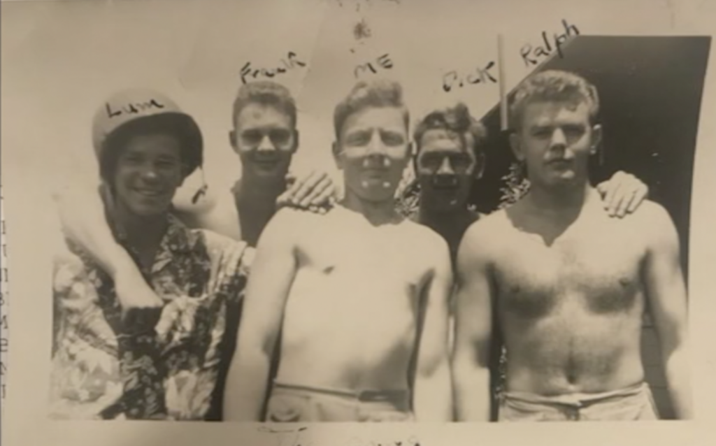 A black and white photo with five young White men. One is in uniform. The other are shirtless.
