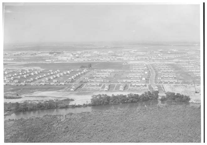 A black and white aerial photo of several rows of housing built in the middle of large field.