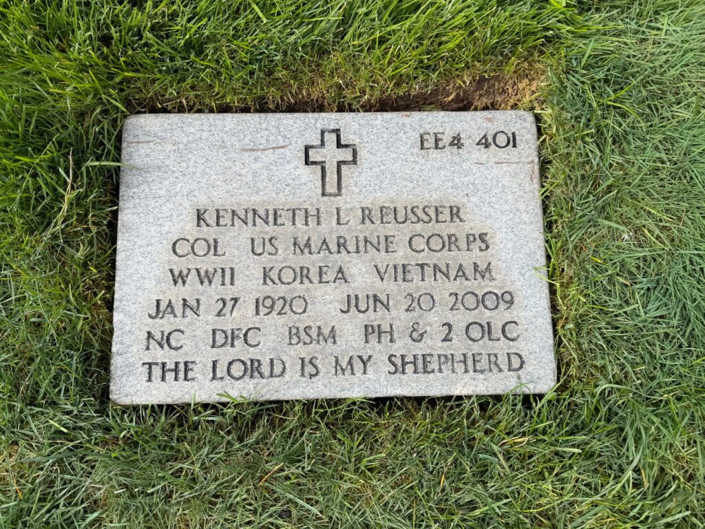 A flat headstone engraved with a cross and the words, “Kenneth L. Reusser COL US Marine Corps WWII Korea Vietnam Jan 27 1920 Jun 20 2009 NC DFC BSM PH & 2 OLC The Lord is My Shepherd.”