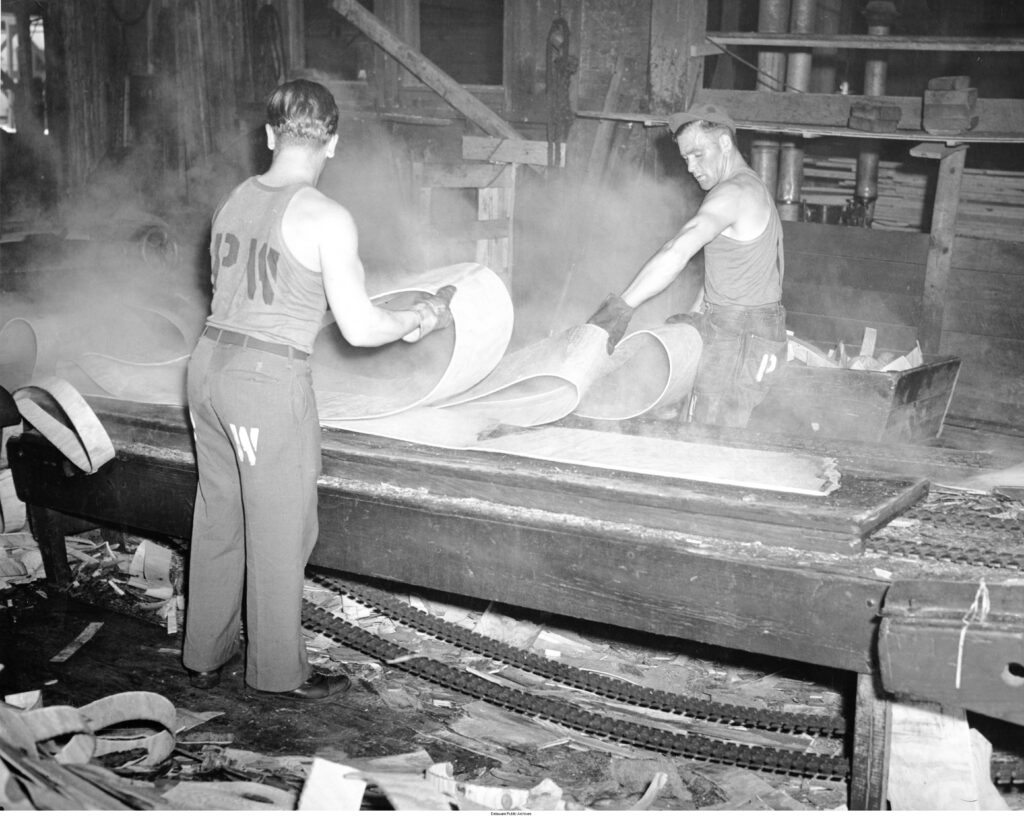 A black and white photo of two men working in a factory.