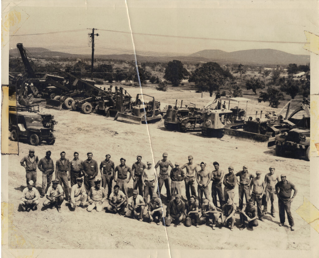 A black and white aerial image of a group of young White Marines in a field in front of equipment.