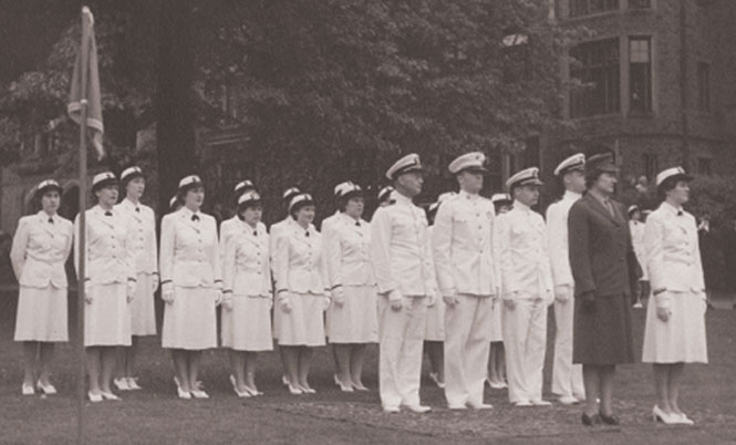 A black and white photo of several men and women in uniform outside a dorm building.