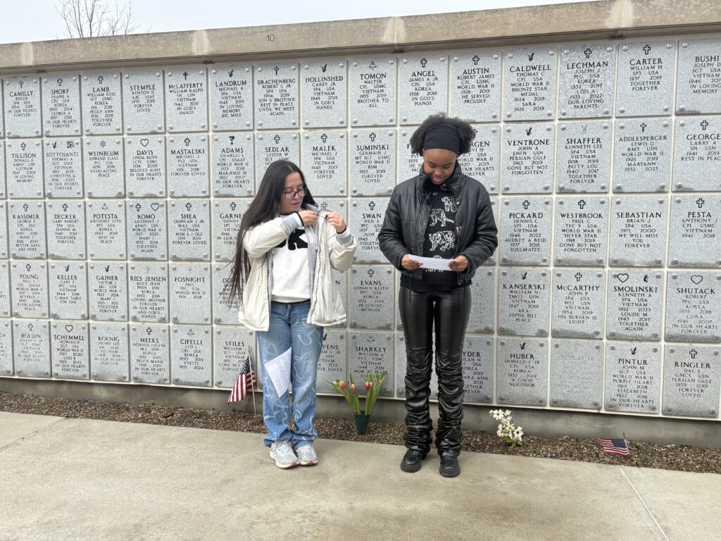Two girls stand in front of a wall of engraved markers.