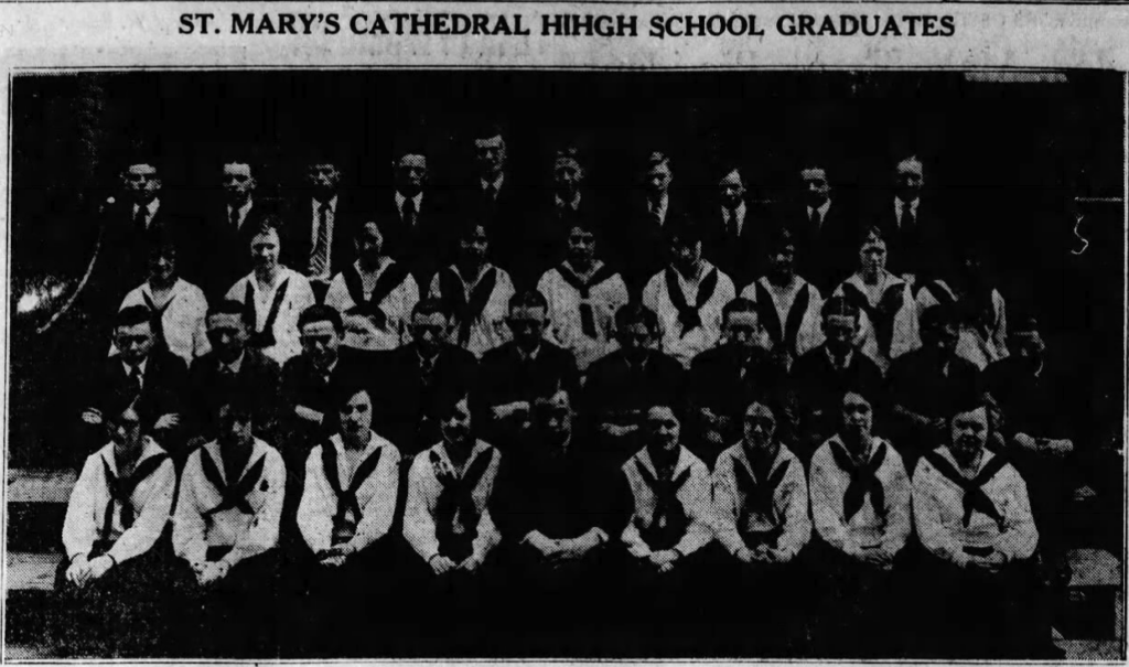 A black and white image of a high school class posing. The boys are in suits, and the girls are wearing white button-up shirts with black sailor ties. 
