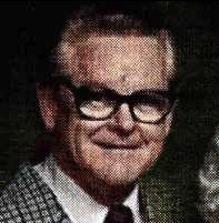 A color headshot picture of an older White man in black glasses and a suit and tie.