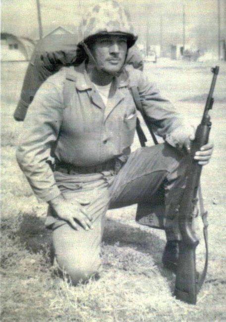 A black and white photo of a White man in a Korean-era uniform. He is down on one knee and holding a rifle.