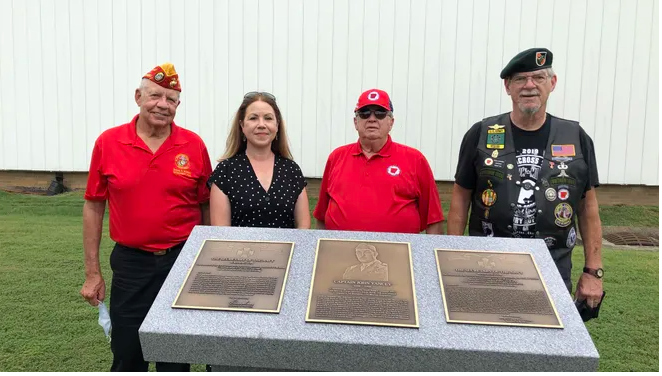 Four people stand behind a marble podium with three bronze plaques on top.