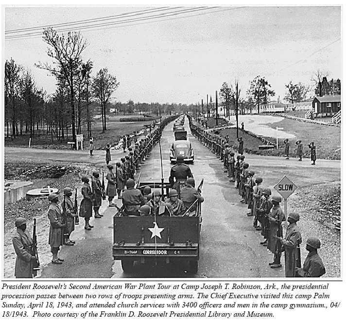 A black and white image of a long line of cars driving down a road with soldiers standing at attention on either side.