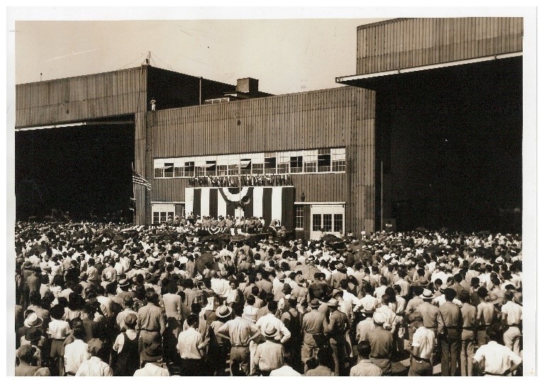 A black and white photograph of hundreds of people gathered outside a building in the street. 