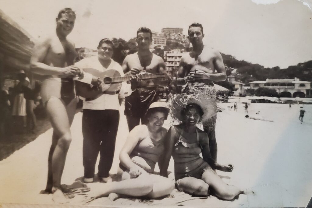 A black and white image of several people sitting on a beach.