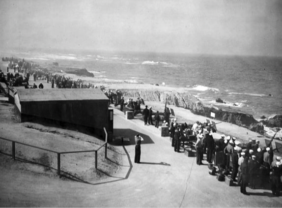 A black and white image of dozens of soldiers on the rocky coast.