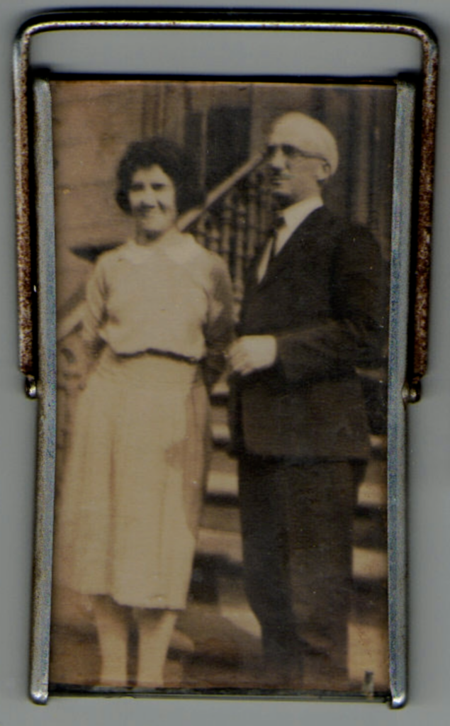 A black and white photo of an older White couple standing outside a home.