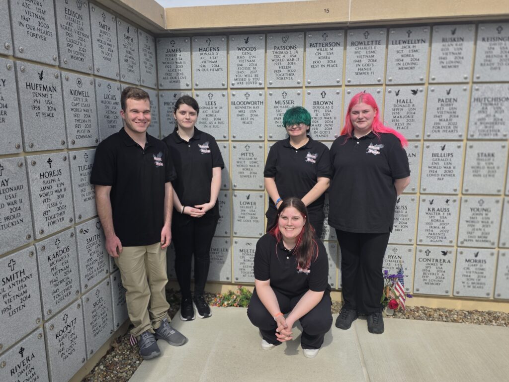 A color image of several students standing in front of a wall of gravestones.