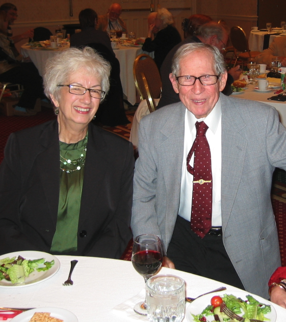 An elderly White couple dressed up sitting at a table.