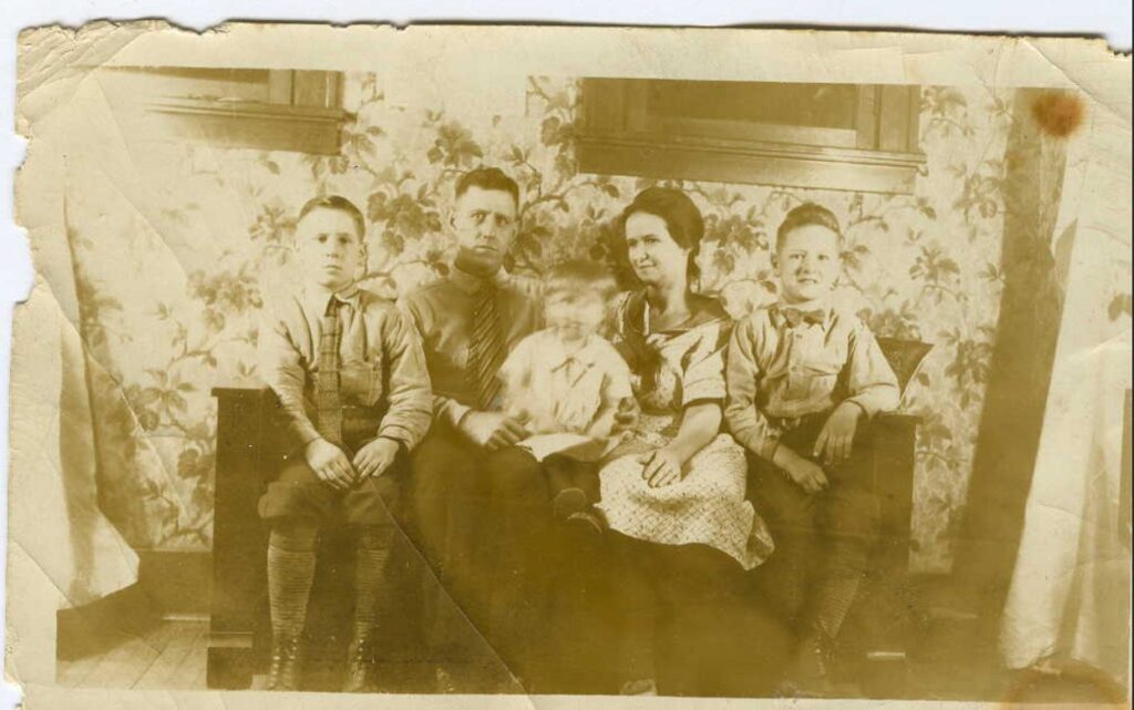 A sepia-toned photograph of a young White family sitting on a couch with three children.
