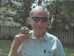 A color photograph of an elderly man holding a turtle figure.