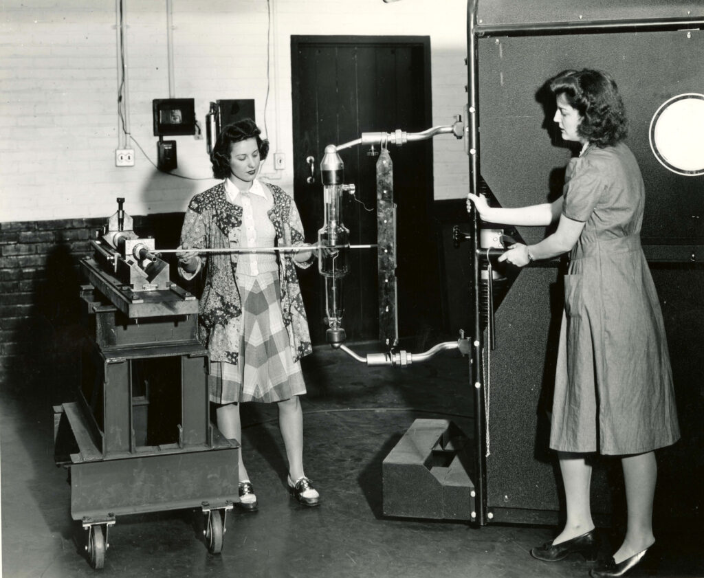 A black and white photograph of two women experimenting on a gun barrel.