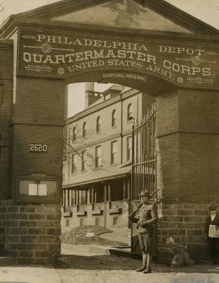 A black and white image of a large brick arched entrance with an armed guard outside.