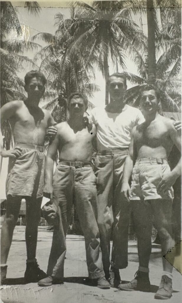 A black and white photo of four young White men standing underneath palm trees.