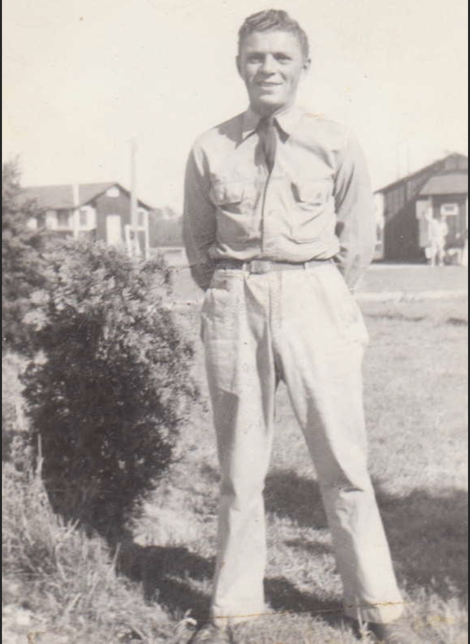 A black and white full-length image of a young man in a uniform.