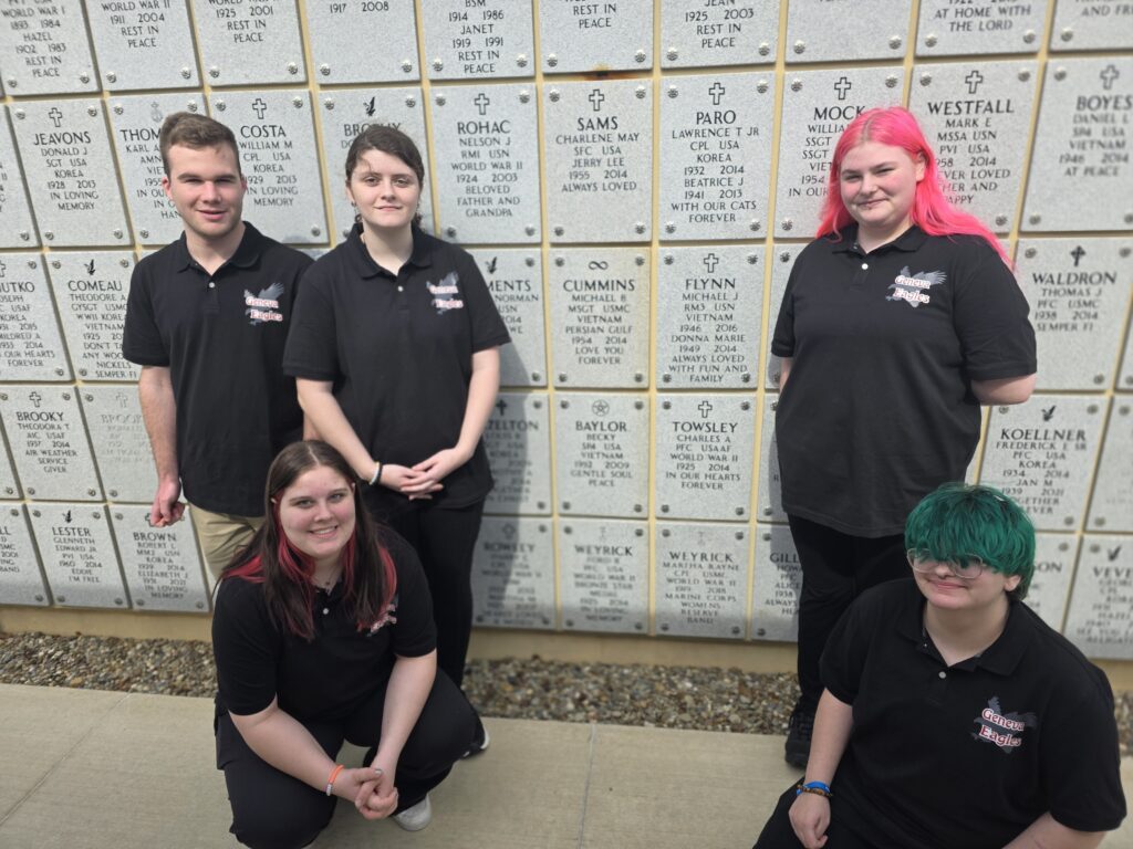 A color photo of several students standing in front of a wall of gravestones.