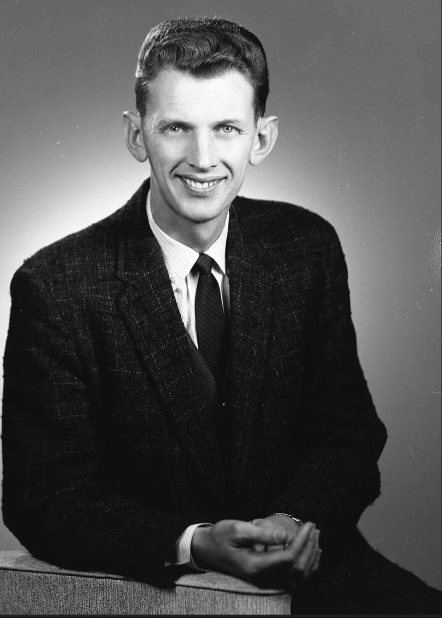 A black and white image of a White man in a suit and tie from the waist up.